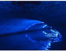 Unterirdischer Tunnel oder Gewölbe mit bläulicher Beleuchtung, die sich auf der Wasseroberfläche spiegelt. Die gewölbte Decke und die reflektierenden Lichtlinien dominieren die Szenerie.
