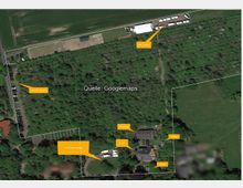 Luftaufnahme eines bewaldeten Geländes mit verschiedenen markierten Bereichen, darunter ein Catering-Bereich mit Zelten, ein Parkplatz für Crew-Mitglieder, ein Technik- oder Parkplatzbereich, ein Stallgebäude und mehrere Pavillons. Das Gelände ist von Bäumen umgeben, mit angrenzenden Feldern im oberen Bereich des Bildes.