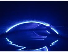 Dunkler Tunnel mit gewölbter Backstein-Decke, beleuchtet durch neonblaue Lichtstreifen, die auf der Wasseroberfläche darunter reflektieren.