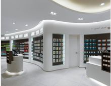 Modernes Apothekeninterior mit abgerundeten weißen Regalen, die mit Medikamenten und Produkten gefüllt sind. Ein geschwungener Empfangstresen steht im Vordergrund, die Umgebung ist hell beleuchtet mit einem minimalistischen Design.