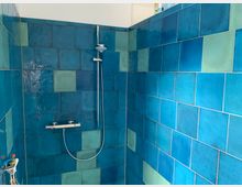 Dusche mit blau-grünen Wandfliesen in quadratischem Muster und einer silbernen Duscharmatur mit Handbrause.