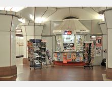 Kleiner Kiosk in einer U-Bahn-Station mit dem Schriftzug "Altstadt Spandau" an der Wand. Der Kiosk ist von Zeitschriftenständern umgeben und bietet Artikel sowie Getränke an, erkennbar durch ein beleuchtetes Schild mit der Aufschrift "Coffee".