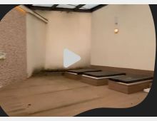 Ein kleiner, eingeschlossener Außenbereich mit Holzterrasse, drei rechteckigen Lichtschächten und einem transparenten Dach. Die Wände sind hell gestrichen, und eine Außenleuchte ist an der Wand angebracht.