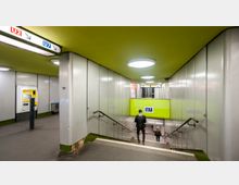 U-Bahn-Station mit grün gestrichenem Deckenbereich und weißen Metallwänden. Im Vordergrund führt eine Treppe mit Handläufen zum Bahnsteig der Linie U7 hinunter, daneben ein Fahrkartenautomat.