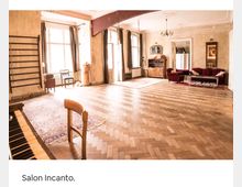 Ein großzügiger Innenraum mit Holzboden im Fischgrätmuster, großen Fenstern mit Vorhängen und einer Mischung aus klassischer und wohnlicher Einrichtung, einschließlich eines Klaviers, Polstermöbeln und Holzmöbeln. Der Raum wirkt hell durch das einfallende Tageslicht.