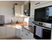 Moderne Küche mit weißen Schränken, einer Holzarbeitsplatte und einer integrierten schwarzen Mikrowelle und Backofen. Fliesen mit gemustertem Design schmücken den Bereich über der Spüle und dem Herd, und eine Zimmerpflanze hängt von einem der Hängeschränke herunter.