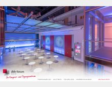 Moderner Kongress- und Tagungsraum mit einer hohen Decke, futuristischer Beleuchtung in Blau- und Lilatönen, weißen Stehtischen und einer farbig beleuchteten Wand mit kreisförmigem Muster. Im Hintergrund sind Glaswände, ein Treppenaufgang und eine Galerie sichtbar.