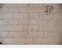 Alter, beige gefliester Wand mit rechteckigen, glasierten Fliesen, die Risse, kleine Verfärbungen und Spuren von Abnutzung aufweisen. Die Fugen sind weiß und teilweise unregelmäßig gestaltet.