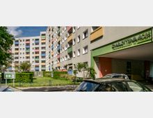 Mehrstöckiges Wohngebäude mit farbigen Balkonen und einem gepflegten Grünbereich im Vordergrund. Der Schriftzug „Charlottenburger Baugenossenschaft eG“ ist über einem überdachten Eingangsbereich sichtbar.