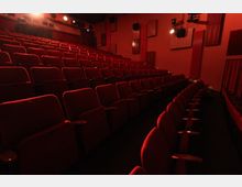 Innenansicht eines kleinen Kinos mit mehreren Reihen roter Sitzplätze. Die Wände sind ebenfalls rot und schallgedämpft, mit Beleuchtung an der Decke und an den Wänden.