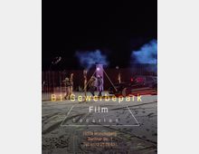 Nachtszene mit einer filmischen Aufnahme auf einer Freifläche, umgeben von Containern und schwachem Kunstlicht. Im Vordergrund ist Schnee mit Reifenspuren und Personen sowie ein schwarzes Auto zu sehen, während blauer Rauch im Hintergrund aufsteigt. Textinformationen auf dem Bild geben Standort und Kontakt für die Film-Location "B1 Gewerbepark" in Müncheberg an.