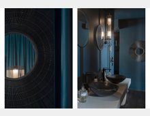 Dunkel gehaltenes modernes Badezimmer mit schwarzen, runden Waschbecken auf einer hellen Arbeitsplatte, runden Spiegeln an der Wand und minimalistischen Wandlampen. Die Wände und Dekorelemente sind in dunklen Blau- und Schwarztönen gehalten.