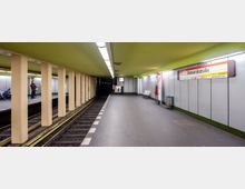 U-Bahnhof mit gelb-grüner Decke und einer einfachen Betonarchitektur, durchzogen von gelben Säulen. Ein Bahnsteig mit Sitzbänken, Wandschildern, einer Uhr und einem Hinweisschild mit der Aufschrift „Bismarckstraße“.