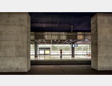 Unterirdischer Bahnhof mit modernen, beleuchteten Glaswänden, breiten Betonsäulen und einem Schild mit der Aufschrift „Potsdamer Platz“. Ein Aufgang mit Rolltreppe und eine Uhr sind im Hintergrund sichtbar.