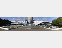 Weitwinkelfoto eines modernen Gebäudes mit markanten weißen, gefalteten Dachstrukturen, flankiert von symmetrischen Wasserspielen mit Springbrunnen im Vordergrund. Im Hintergrund ist der Berliner Fernsehturm zu sehen, umgeben von Bäumen und freiem Himmel.