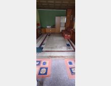 Wohnzimmer mit grüner Wand, einer hölzernen Rückwand und möbliert mit einem roten Sofa, einem niedrigen Holzschrank und einer Schrankwand mit Schiebetüren. Der Boden ist mit einem großen gemusterten Teppich und kleineren Teppichvorlegern in Pastellfarben gestaltet.