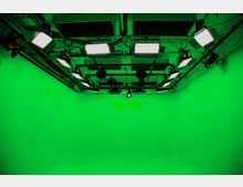 Ein grüner Raum mit glatten Wänden und einer Hohlkehle (Green Screen Studio), beleuchtet durch mehrere an der Decke montierte Studiolampen. Die Szene ist für Film- oder Fotoaufnahmen mit digitaler Hintergrundbearbeitung vorbereitet.