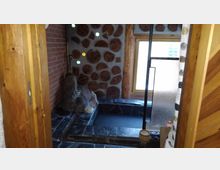 Kleines Badezimmer mit rustikalem Design, Holzwänden und runden Holzscheiben in der Wanddekoration. Im Raum befinden sich Natursteine, ein eingelassenes Becken und ein Fenster mit Milchglas für Lichtdurchlass.