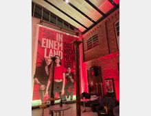 Innenraum eines Kinos mit Backsteinwänden, einer großen Filmplakat-Werbung und roten Lichtakzenten. Im Vordergrund sind Tische, Stühle und Sofas zu sehen, während im Hintergrund der Eingang zu „Kino 5“ hervorsticht.