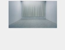 Ein leerer, rechteckiger Raum mit weißen Wänden, einem grauen Bodenbelag und einem großen, bodenlangen Vorhang aus weißen Stoffbahnen an der Rückwand.