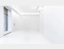 Weißer, minimalistisch gestalteter Innenraum mit hoher Decke, glatten Wänden und einem großen Fenster mit goldfarbenem Rahmen auf der linken Seite. Deckenleuchten sorgen für gleichmäßige Beleuchtung, während die Umgebung leer wirkt.