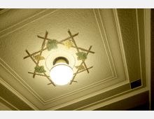 Deckenleuchte in einem Innenraum, umgeben von dekorativen Mosaiken aus Weinreben und Traubenmotiven auf einer strukturierten, rechteckig gerahmten Decke.