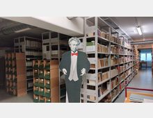 Ein Archivraum mit hohen Metallregalen, die dicht mit Ordnern, Büchern und Archivboxen gefüllt sind. Im Vordergrund steht ein lebensgroßer Pappaufsteller einer historischen Figur in Frack und roter Fliege, und im Hintergrund ist ein Fenster mit Tageslichteinfall sichtbar.