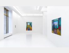 Minimalistischer Ausstellungsraum mit weißen Wänden und glänzendem Boden. An den Wänden hängen moderne Gemälde in kräftigen Farben, und links ist ein großes Fenster mit schmalem Rahmen sichtbar, das Tageslicht hineinlässt.