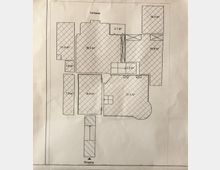 Grundriss eines Gebäudes mit mehreren Räumen, die in Quadratmetern beschriftet sind. Der Plan zeigt Bereiche wie eine Terrasse (oben), einen Eingang (unten) und unterschiedliche Raumgrößen, gekennzeichnet durch schraffierte Flächen.