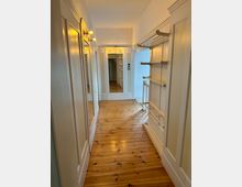 Schmaler Flur mit hellem Holzboden, weiß gestrichenen Wänden und maßgefertigten Einbauschränken mit Spiegeln. An der Decke befinden sich mehrere kleine Leuchten, die den Raum gleichmäßig beleuchten.