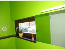 Kleines Badezimmer mit hellgrünen Wänden, einem schmalen Fenster mit dunklem Holzrahmen und einer Fensterbank. Auf der Fensterbank stehen ein kleiner Kaktus in einem gelben Topf und eine kleine Tube, die sich vor einem großen Spiegel befinden.