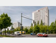 Hochhäuser mit weißer Fassade und großen Fenstern an einer Kreuzung, umgeben von Bäumen und Straßenverkehr mit Autos und einem Transporter; ein Straßenschild weist die "Eisenacher Straße" aus.