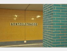 U-Bahn-Station mit einer gelben Kachelwand, auf der in schwarzen Buchstaben der Stationsname „Güntzelstraße“ steht; rechts im Vordergrund eine mit türkisfarbenen Kacheln verkleidete Säule.