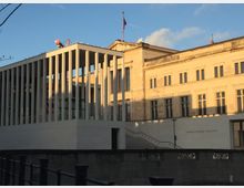 Moderne Museumsarchitektur: Vorderansicht der James-Simon-Galerie in Berlin. Das Bild zeigt das helle Gebäude mit schlanken Säulen sowie ein angrenzendes historisches Bauwerk im warmen Licht der untergehenden Sonne.