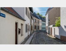 Eine schmale, gepflasterte Straße mit historischen Wohnhäusern auf beiden Seiten, typischen Satteldächern und schlichten Fassaden. Eine Laterne steht am rechten Straßenrand, und der Straßenname „Mauerstraße“ ist auf einem Schild links erkennbar.