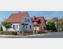 Reihen von Einfamilienhäusern mit roten Satteldächern in einer ruhigen Wohnstraße, umgeben von kleinen Vorgärten, Zäunen und Bäumen; ein Straßenschild mit der Aufschrift „Hamburger Straße“ ist sichtbar.