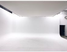 Großes, leeres Fotostudio mit komplett weißen, nahtlosen Wänden, Boden und Decke. Eine dunkle Öffnung führt zu einem angrenzenden Raum auf der rechten Seite.
