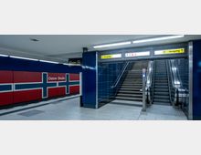 U-Bahn-Station mit dem Schriftzug "Osloer Straße" an einer Wand, die in den Farben der norwegischen Flagge gestaltet ist. Im Vordergrund befinden sich ein Treppenaufgang und eine Rolltreppe, darüber leuchtet ein Schild mit der Markierung "Ausgang".