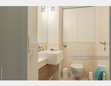 Kleines modernes Badezimmer mit hellen Fliesenwänden, einem weißen Waschbecken mit Holzunterschrank, einem wandhängenden WC und einem Spiegel mit integriertem Licht. Rechts befindet sich eine Badewanne mit einem blauem Handtuch.