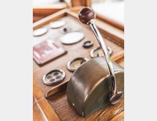 Nahaufnahme eines Vintage-Bedienpults mit Holz- und Metallverkleidung. Im Vordergrund ist ein glänzender Hebel mit Holzgriff zu sehen, umgeben von analogen Anzeigen und Steuerinstrumenten.