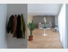 Modernes, minimalistisch gestaltetes Wohnzimmer mit hellen Holzfußböden und cremefarbenen Wänden. Im Vordergrund ein runder Tisch mit einer grünen Vase, einem Dekorationsobjekt und ein großer Kaktus in einem Terrakottatopf; im Hintergrund eine graue Küchenzeile und helle bodenlange Vorhänge.