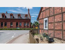 Zweifamilienhaus (Fachwerkstil rechts) mit Ziegelmauern und verzierter Ziegelbau (links). Kiesstraße im Vordergrund.