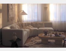 Sunlit modern living room with a white sectional sofa, textured throw blankets and pillows, and an arched floor lamp beside large windows with sheer curtains. A low oval wooden coffee table sits on a shag rug, with neutral-toned decor and a woven wall hanging on the left wall.