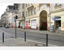 Straßenszene mit mehrstöckigen Altbauten an der Ecke Rosenstraße und Kietzer Straße. Fassaden der Gebäude sind zum Teil mit Graffiti besprüht, Schilder und Leuchtreklamen hängen an den Fenstern, und Pflastersteine bedecken den Gehweg und die Straße mit Straßenbahnschienen.