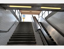 Treppenaufgang und Rolltreppe in einer U-Bahn-Station mit weißen, gefliesten Wänden; oben sichtbar ist ein Schild mit dem blauen "U" und der Liniennummer U3.