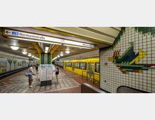U-Bahn-Station der Linie U8 in Berlin mit gelber, einfahrender U-Bahn; Wandfliesen zeigen ein Mosaik eines bunten Vogels. Der Bahnsteig ist mit gelb-grünen Säulen, Leuchtkörpern und weiß-beige gemusterten Fliesen gestaltet, einige Personen sind zu sehen.