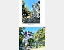 Außenansicht eines modernen Gebäudes mit weißer Fassade und roten Akzenten, umgeben von Bäumen. Im Vordergrund sind ein gepflasterter Weg, ein Zaun mit Tor und ein kleiner Gartenbereich sichtbar.