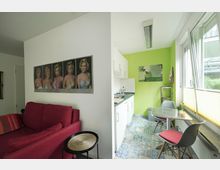 Kompakte Wohnung mit kombiniertem Wohn- und Essbereich. Links steht ein rotes Sofa vor einer weißen Wand mit Portraits auf einem Poster, rechts eine kleine Küchenzeile, ein Esstisch mit Stühlen und grün gestrichene Wände mit großen Fenstern.