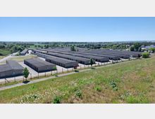 Weitläufiges Gelände mit mehreren Reihen flacher, rechteckiger Lagergebäude aus Beton, die von einem Zaun umgeben sind. Im Hintergrund befinden sich Felder, Bäume und vereinzelte Gebäude in einer ländlichen Umgebung.
