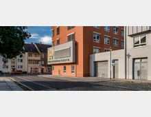 Straßenecke in einer städtischen Umgebung mit einem markanten, orangefarbenen Gebäude namens "Fürstengalerie". Das Gebäude besitzt moderne Fensterfassungen, ein auffälliges Werbeschild und angrenzend befinden sich weitere Wohn- und Geschäftshäuser.